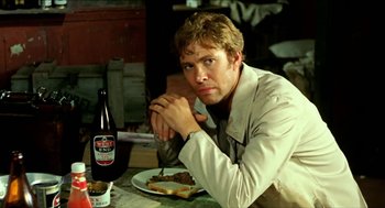 Movie still from “Wake in Fright” (1971), directed by Ted Kotcheff – A man sitting in front of a plate of food; Medium shot, Low angle