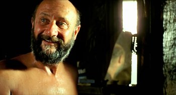 Movie still from “Wake in Fright” (1971), directed by Ted Kotcheff – A man with a beard is smiling for the camera; Close Up shot, Over the shoulder angle