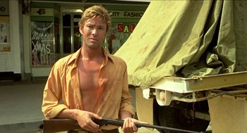 Movie still from “Wake in Fright” (1971), directed by Ted Kotcheff – A man holding a rifle while standing in front of a truck; Medium shot, Low angle