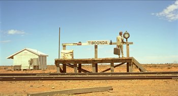 Movie still from “Wake in Fright” (1971), directed by Ted Kotcheff – A man standing on top of a wooden platform near train tracks; Extreme Wide shot, Low angle
