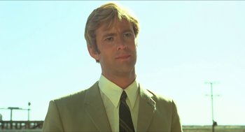 Movie still from “Wake in Fright” (1971), directed by Ted Kotcheff – A man wearing a suit and tie in front of a sky background; Close Up shot, Low angle