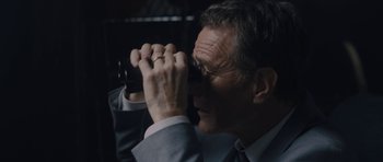 Movie still from “Wakefield” (2016), directed by Robin Swicord – A man in a suit looking through binoculars; Close Up shot, High angle