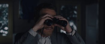 Movie still from “Wakefield” (2016), directed by Robin Swicord – A man looking through binoculars while wearing a suit; Close Up shot, Over the shoulder angle