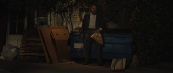 Movie still from “Wakefield” (2016), directed by Robin Swicord – A man holding a tennis racquet sitting next to a dumpster; Wide shot, Low angle