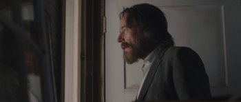 Movie still from “Wakefield” (2016), directed by Robin Swicord – A man with long hair and a beard looking out of a window; Close Up shot, Over the shoulder angle