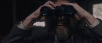 Movie still from “Wakefield” (2016), directed by Robin Swicord – A man with a beard looking through a pair of binoculars; Close Up shot, Over the shoulder angle