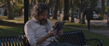 Movie still from “Wakefield” (2016), directed by Robin Swicord – A man sitting on top of a park bench reading a book; Medium shot, Over the shoulder angle
