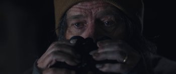 Movie still from “Wakefield” (2016), directed by Robin Swicord – An older man looking through binoculars in the dark; Close Up shot, Over the shoulder angle