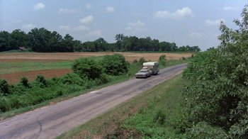 Movie still from “Walking Tall” (1973), directed by Phil Karlson – A truck driving down a road near a field of grass; Extreme Wide shot, High angle