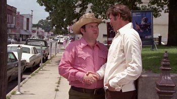 Movie still from “Walking Tall” (1973), directed by Phil Karlson – A man in a cowboy hat shaking hands with another man in a white shirt; Medium shot, Over the shoulder angle