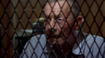 Movie still from “Walking Tall” (1973), directed by Phil Karlson – An old man wearing glasses sitting in front of a chain link fence; Close Up shot, High angle