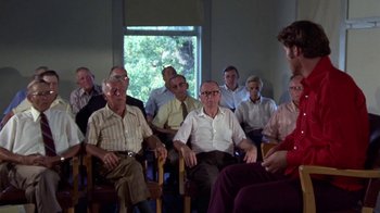 Movie still from “Walking Tall” (1973), directed by Phil Karlson – A group of people sitting in chairs in a room; Wide shot, Over the shoulder angle