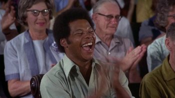 Movie still from “Walking Tall” (1973), directed by Phil Karlson – A man laughing while sitting next to a group of people; Close Up shot, Over the shoulder angle