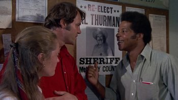 Movie still from “Walking Tall” (1973), directed by Phil Karlson – Two men and a woman talking in front of posters; Medium shot, Over the shoulder angle