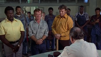 Movie still from “Walking Tall” (1973), directed by Phil Karlson – A group of people standing around a table; Medium shot, High angle