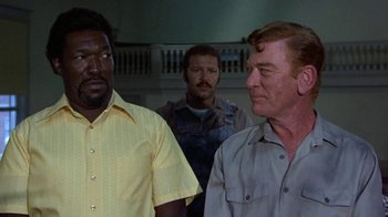 Movie still from “Walking Tall” (1973), directed by Phil Karlson – A group of men standing next to each other in a room; Medium shot, Over the shoulder angle