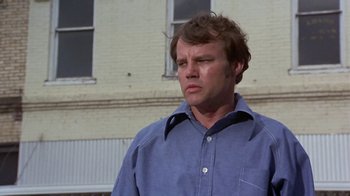 Movie still from “Walking Tall” (1973), directed by Phil Karlson – A man standing in front of a brick building looking to his left; Close Up shot, Low angle