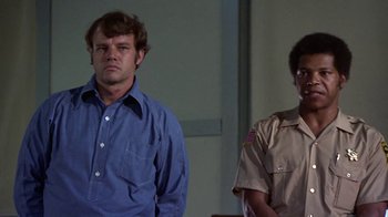 Movie still from “Walking Tall” (1973), directed by Phil Karlson – Two men standing next to each other in front of a wall; Medium shot, Low angle