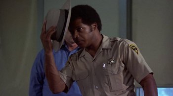 Movie still from “Walking Tall” (1973), directed by Phil Karlson – A man in uniform holding a hat up to his head; Close Up shot, Low angle