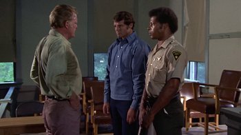 Movie still from “Walking Tall” (1973), directed by Phil Karlson – A group of men standing next to each other in a room; Medium shot, Over the shoulder angle