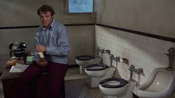 Movie still from “Walking Tall” (1973), directed by Phil Karlson – A man standing next to a row of toilets; Medium shot, High angle