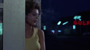 Movie still from “Walking Tall” (1973), directed by Phil Karlson – A woman smoking a cigarette in front of a building; Medium shot, Low angle