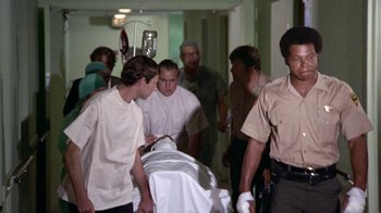 Movie still from “Walking Tall” (1973), directed by Phil Karlson – A group of people in a room with a person on a bed; Medium shot, Low angle