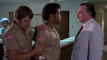 Movie still from “Walking Tall” (1973), directed by Phil Karlson – A man in a suit and tie with two other men in uniform; Medium shot, Low angle