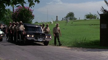 Movie still from “Walking Tall” (1973), directed by Phil Karlson – A group of men standing next to a car on the side of the road; Wide shot, Over the shoulder angle