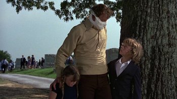 Movie still from “Walking Tall” (1973), directed by Phil Karlson – A man standing next to two children under a tree; Medium shot, Low angle