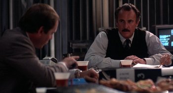 Movie still from “WarGames” (1983), directed by John Badham – Two men are sitting at a table with drinks in front of them; Medium shot, Over the shoulder angle