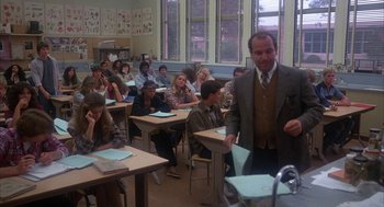Movie still from “WarGames” (1983), directed by John Badham – A man in a suit and tie standing in front of a classroom full of students; Wide shot, High angle