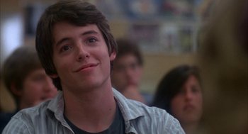 Movie still from “WarGames” (1983), directed by John Badham – A young man smiling while sitting in front of a group of people; Close Up shot, Low angle