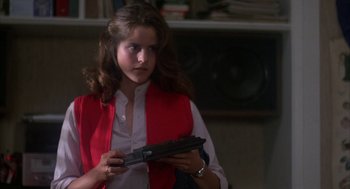 Movie still from “WarGames” (1983), directed by John Badham – A woman in a red vest holding a gun in her hands; Medium shot, Over the shoulder angle