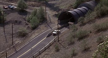 Movie still from “WarGames” (1983), directed by John Badham – An aerial view of a car driving through a tunnel on the side of a road; Extreme Wide shot, High angle