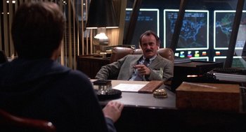 Movie still from “WarGames” (1983), directed by John Badham – A man sitting at a table in front of another man; Medium shot, Over the shoulder angle