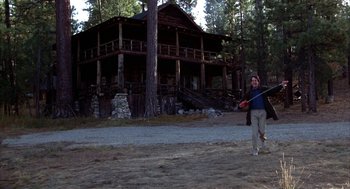 Movie still from “WarGames” (1983), directed by John Badham – A man holding a frisbee in front of a log house; Wide shot, Low angle