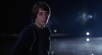 Movie still from “WarGames” (1983), directed by John Badham – A young man is standing in the dark; Medium shot, Over the shoulder angle