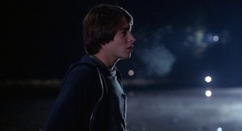 Movie still from “WarGames” (1983), directed by John Badham – A young man is standing in the dark with smoke coming out of his mouth; Close Up shot, Over the shoulder angle