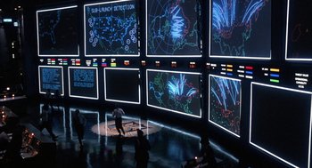 Movie still from “WarGames” (1983), directed by John Badham – A group of people standing in front of a wall of screens; Extreme Wide shot, High angle