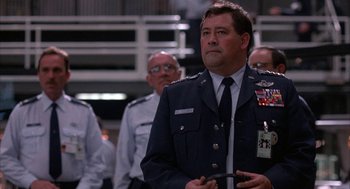 Movie still from “WarGames” (1983), directed by John Badham – A man in a military uniform standing in front of a group of people; Close Up shot, Low angle