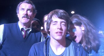 Movie still from “WarGames” (1983), directed by John Badham – A group of people standing around a man with headphones on; Close Up shot, Over the shoulder angle