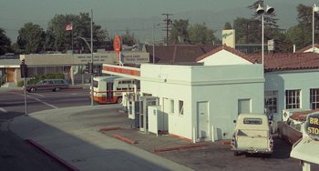 Movie still from “Watermelon Man” (1970), directed by Melvin Van Peebles – An orange and white bus parked at a gas station; Extreme Wide shot, High angle