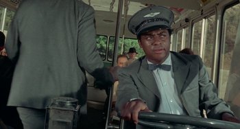 Movie still from “Watermelon Man” (1970), directed by Melvin Van Peebles – A man wearing a hat sitting on a bus; Medium shot, Low angle