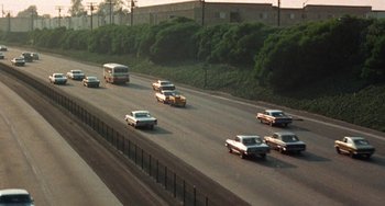 Movie still from “Watermelon Man” (1970), directed by Melvin Van Peebles – Cars are driving down a highway with a bus in the foreground; Extreme Wide shot, High angle