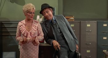 Movie still from “Watermelon Man” (1970), directed by Melvin Van Peebles – A man and a woman standing next to each other in a room; Medium shot, Low angle