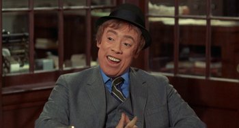 Movie still from “Watermelon Man” (1970), directed by Melvin Van Peebles – A man wearing a suit and a hat is sitting in a chair; Close Up shot, High angle