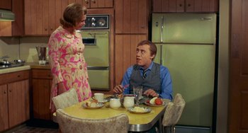 Movie still from “Watermelon Man” (1970), directed by Melvin Van Peebles – A man and a woman sitting at a table in a kitchen; Medium shot, High angle