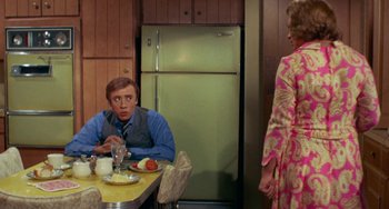 Movie still from “Watermelon Man” (1970), directed by Melvin Van Peebles – A man sitting at a dinner table with a woman; Medium shot, Over the shoulder angle