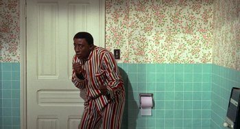 Movie still from “Watermelon Man” (1970), directed by Melvin Van Peebles – A man standing in front of a bathroom stall; Medium shot, High angle